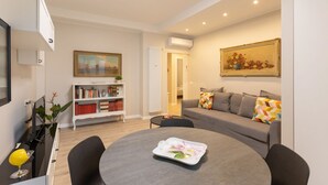 Uma sala de estar moderna com uma mesa de jantar redonda, um sofá cinza e uma estante de livros.