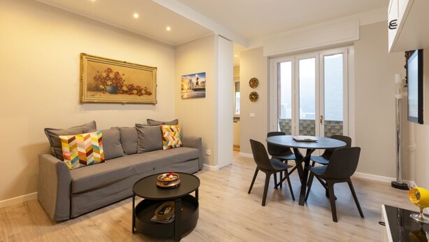 Uma sala de estar moderna com um sofá cinzento, uma mesa de centro e um espaço de jantar com uma mesa redonda e cadeiras.