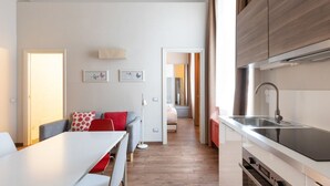 Una cocina moderna con un lavamanos y armarios, un comedor con mesa y sillas, y un pasillo que conduce a un dormitorio.