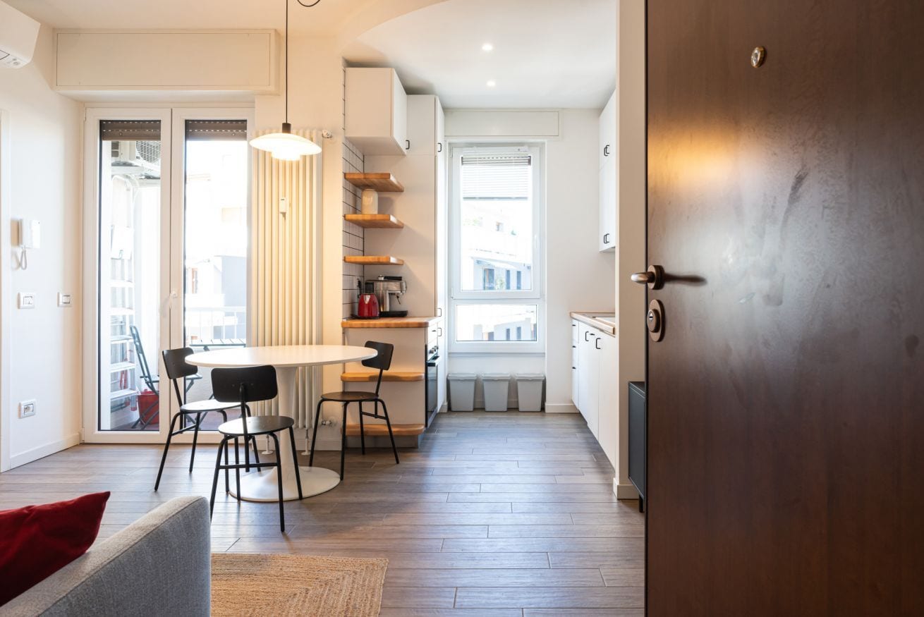 A modern kitchen with a dining area, wooden flooring, and a view through a window.