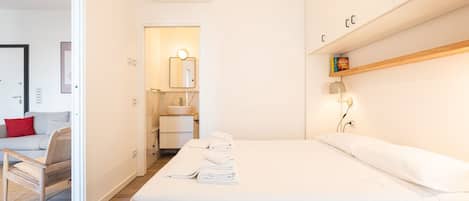 A modern hotel room with a large bed, a bedside table, a mirror, and a small bathroom.