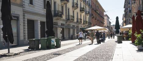 Calle peatonal flanqueada por edificios, con mesas al aire libre y contenedores de basura.