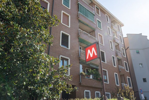 A multi-story building with a prominent red 'M' sign, balconies, and a brick facade.
