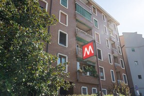 A multi-story building with a prominent red 'M' sign, balconies, and a brick facade. - Modern one bedroom Navigli - Mirable PM (Milano)