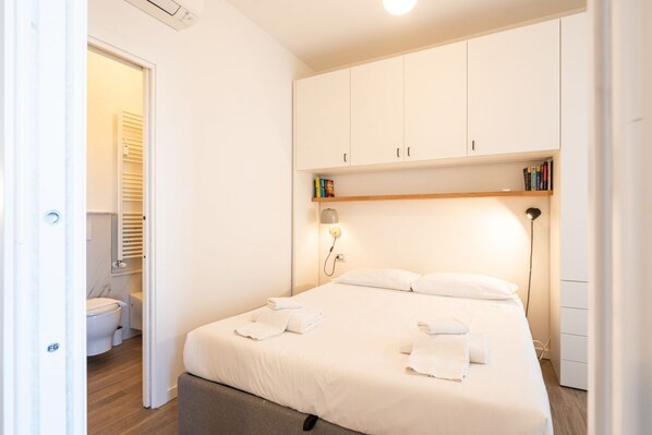 Un dormitorio con cama, lámparas de noche, un armario y una pequeña estantería con libros.