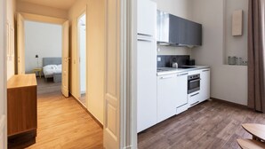 A modern kitchen with white cabinets, a stove, and a microwave. There is a wooden floor and a small dining table.