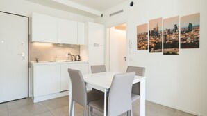 A modern kitchen with white cabinets and a dining area with a white table and four chairs. There are cityscape paintings on the wall. - Charmant onebedroom Isola A (Milano)