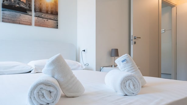A hotel room with a neatly made bed, two rolled towels, a lamp, and a door. - Charmant onebedroom Isola A (Milano)