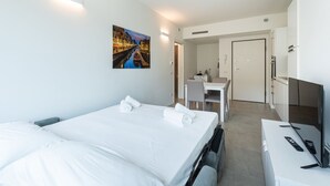 A hotel room with a bed, a desk with a TV, a chair, and a painting on the wall.