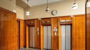 A lobby with wooden paneling, a clock, and three elevators.