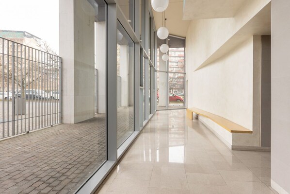 A modern building corridor with glass walls, a tiled floor, and a bench.