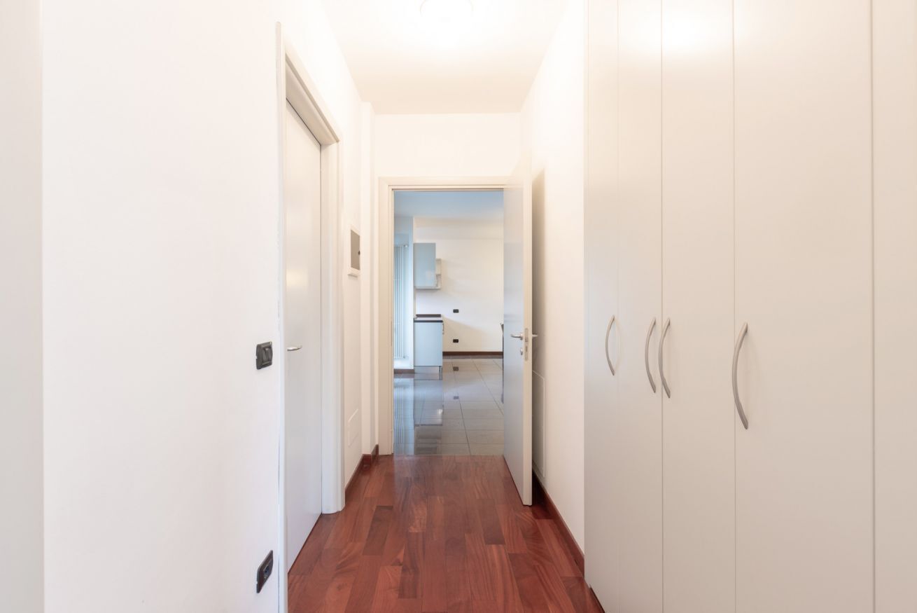 A narrow hallway with wooden flooring leading to a kitchen area.
