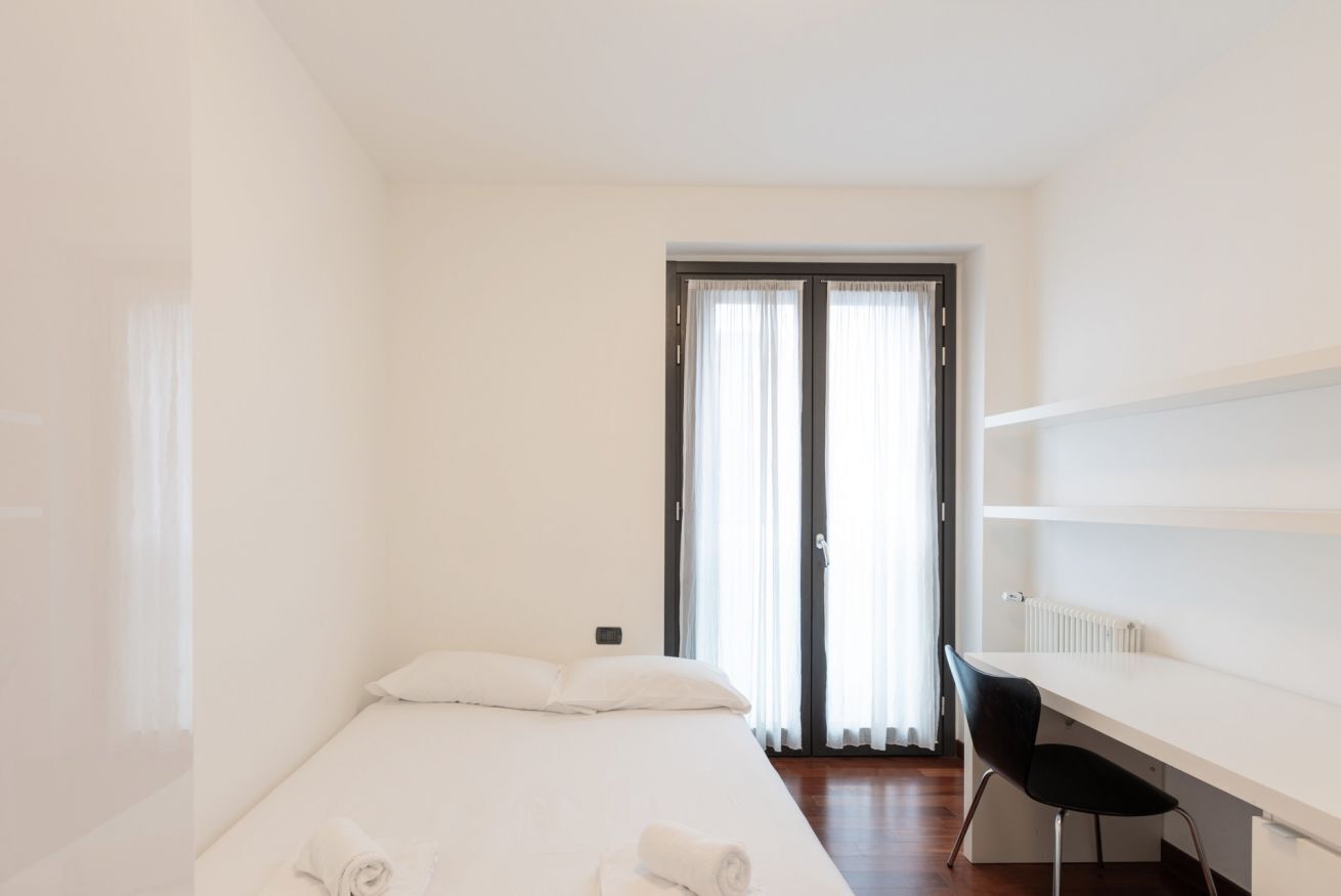 A minimalist hotel room with a bed, a desk, and a chair.
