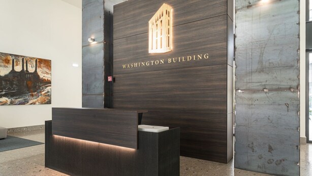 Modernilla designilla varustettu vastaanottotiski, suuri seinä, jossa on teksti ”WASHINGTON BUILDING”, ikkuna ja seinällä oleva taulu.