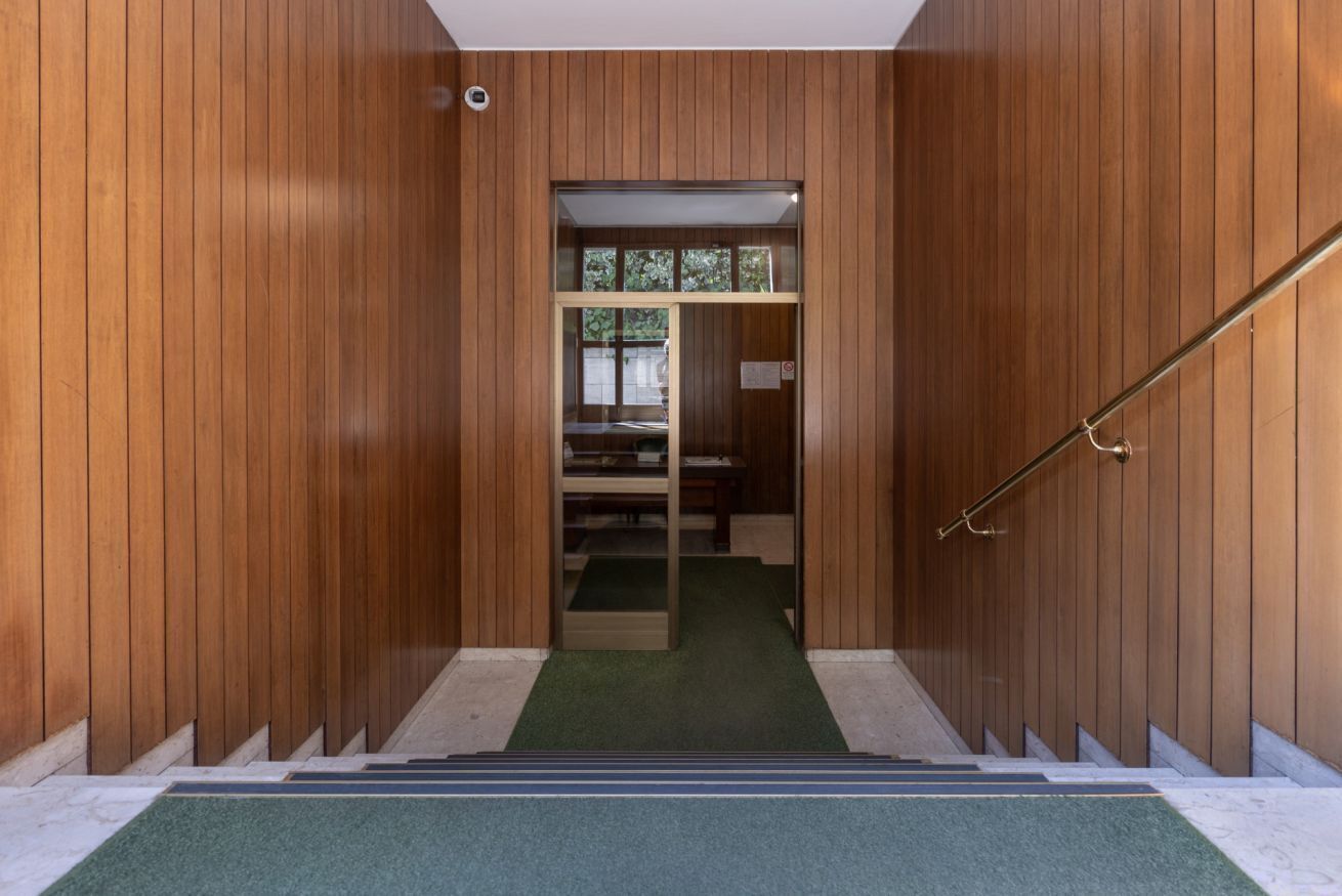 A wooden interior with a staircase leading to a room with a green carpet and a window.