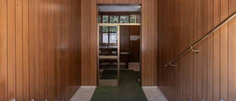 A wooden interior with a staircase leading to a room with a green carpet and a window.