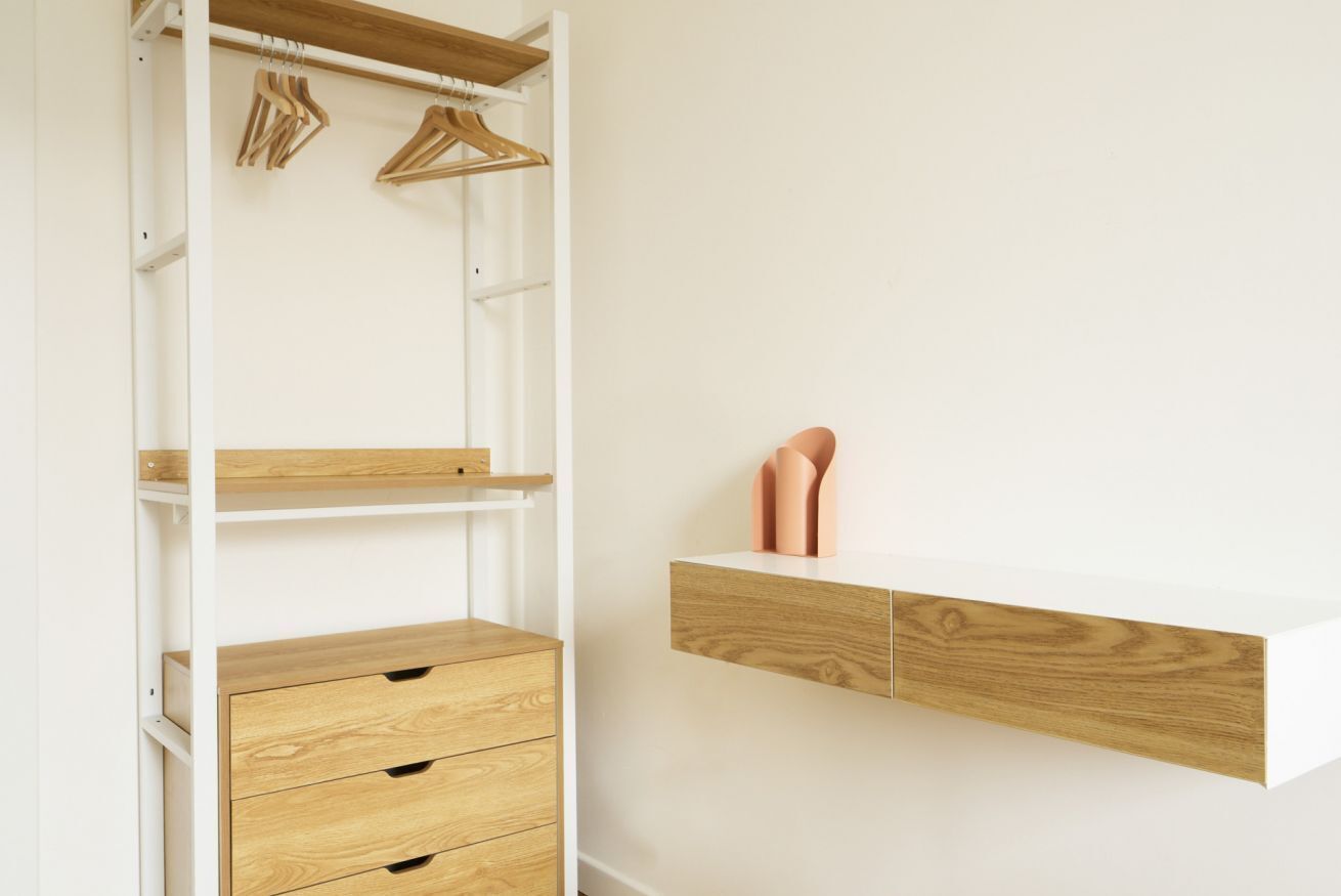 A minimalist closet with wooden shelves, drawers, and a hanging rod.