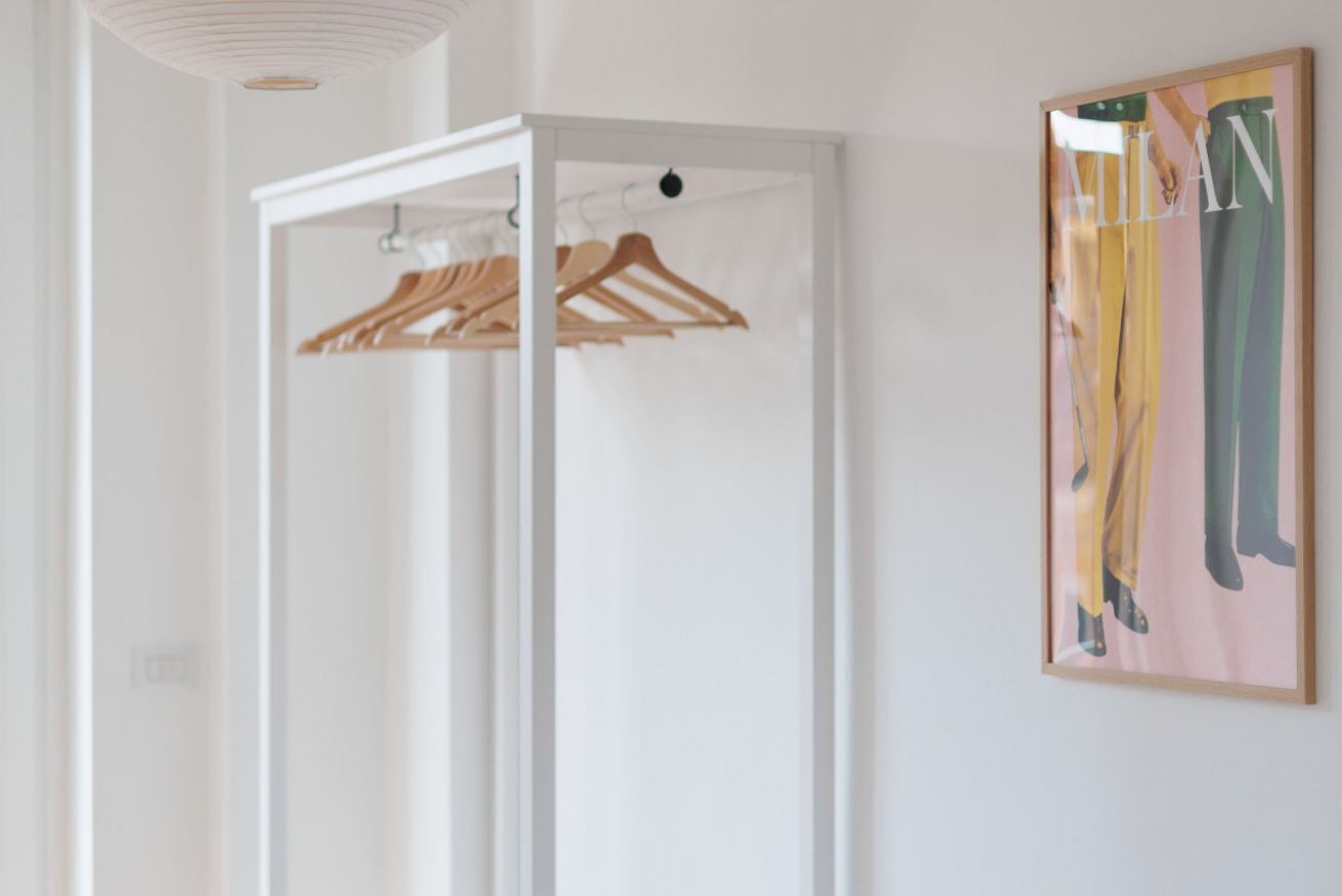A room with a white wardrobe, wooden hangers, and a framed artwork on the wall.