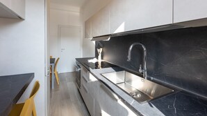A modern kitchen with a black marble backsplash, stainless steel sink, and yellow chairs.