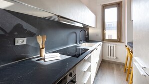 A modern kitchen with a black countertop, stainless steel appliances, and wooden utensils.