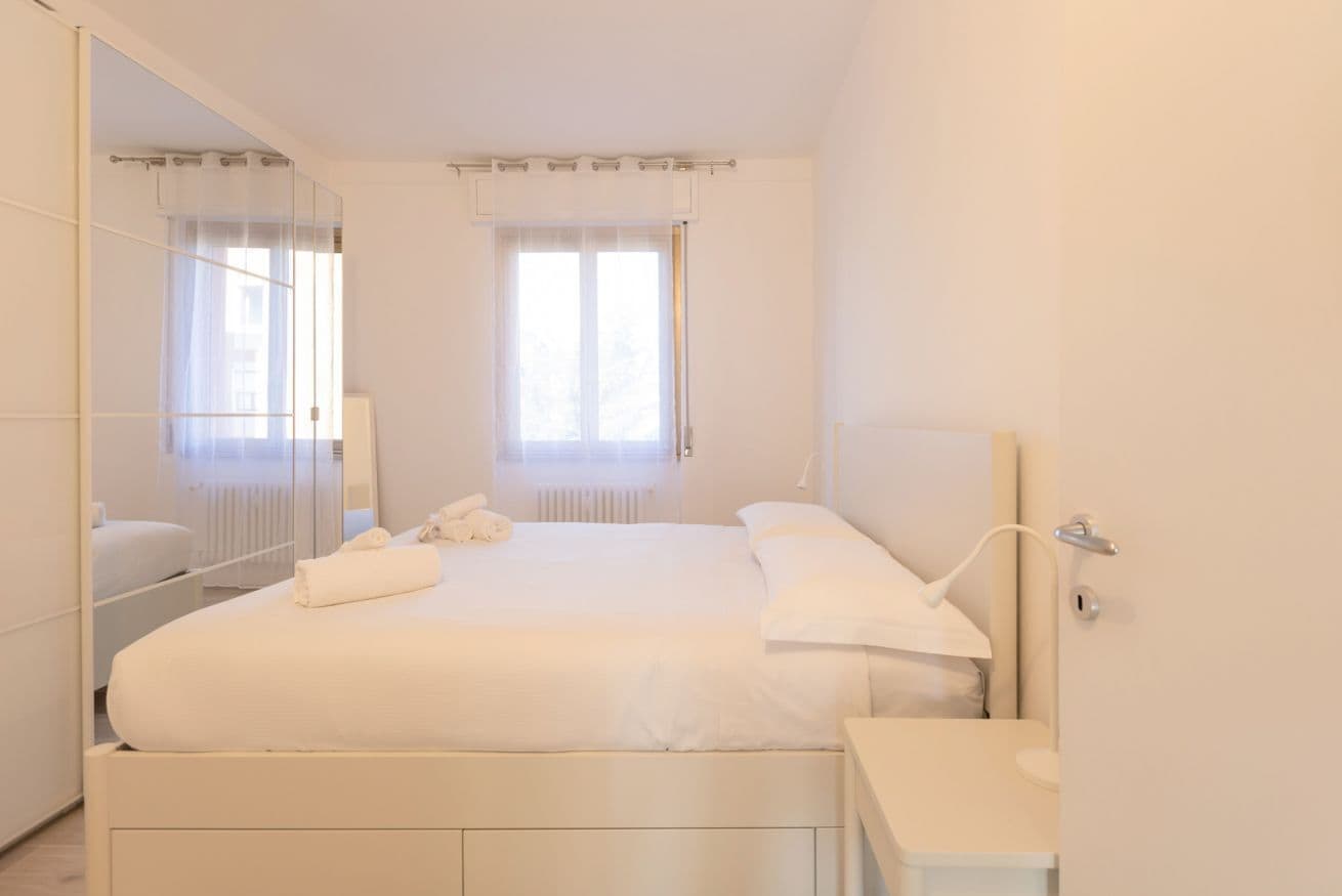 A bedroom with a large bed, a bedside table, a mirror, and a window with curtains.