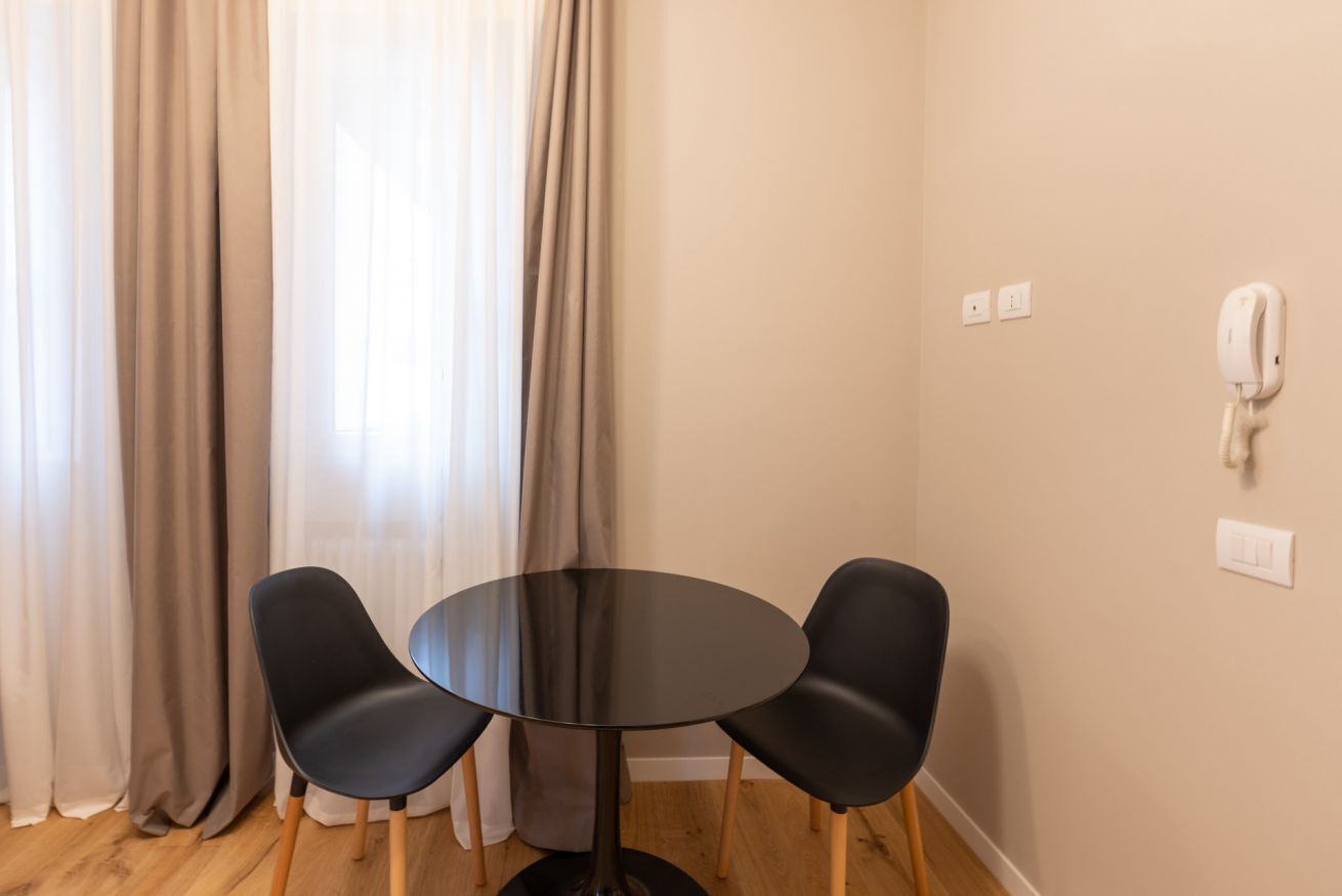 A room with a round table and two chairs, a telephone, and curtains.