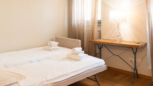 Een hotelkamer met twee bedden, een tafel met lamp en een raam met gordijnen.