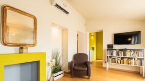 Een woonkamer met een open haard, een boekenkast, een televisie en een fauteuil.