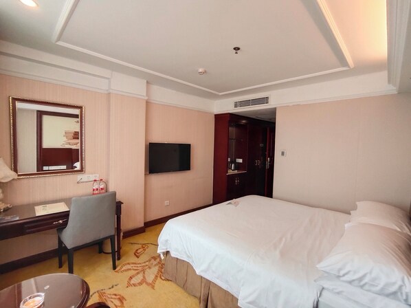 A hotel room with a bed, a desk with a chair, a television, and a mirror.