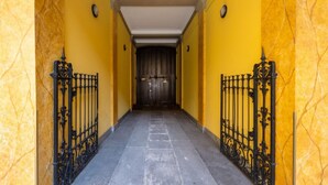 Corredor com paredes amarelas e portões de ferro negro que levam a uma porta de madeira escura.