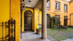 Um edifício amarelo com porta preta, portão de ferro forjado e planta em vaso.