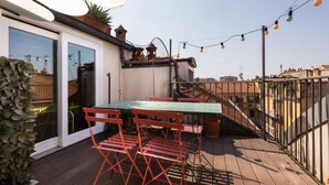 Um terraço no telhado com mesa, cadeiras, luzes de Natal e vista para a paisagem urbana.