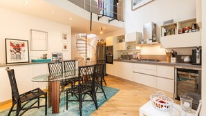 Una cucina moderna con zona pranzo, che include un tavolo in vetro, sedie in vimini e una scala che conduce a un piano superiore.