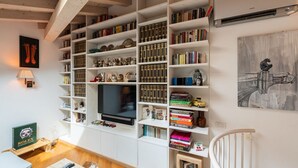 Un soggiorno con un'ampia televisione, mensole piene di libri e un quadro appeso al muro.