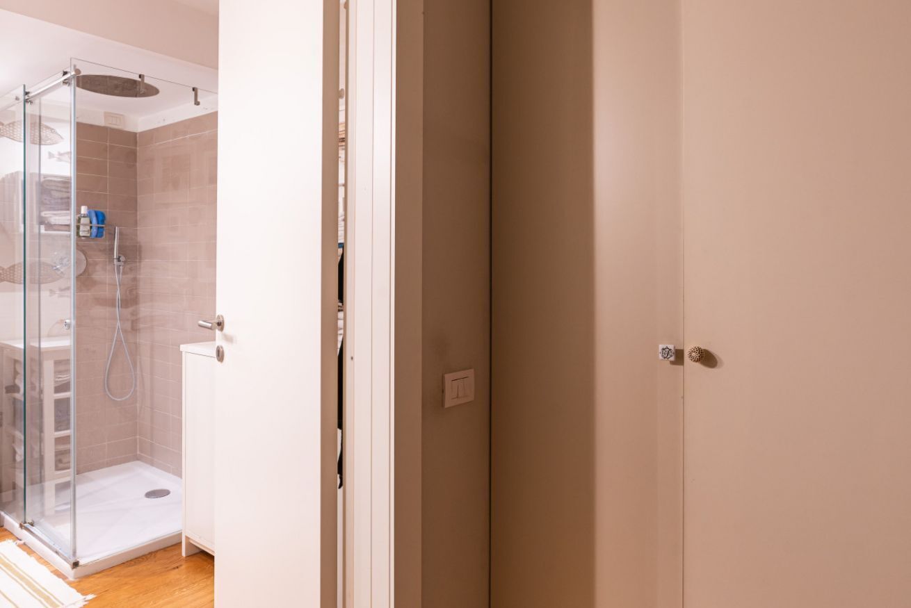 Un baño con cabina de ducha de vidrio, un lavabo blanco y una pared de azulejos color beige.