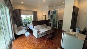 A modern hotel room with a wooden parquet floor, a sofa, a bed, a dining table, and a sliding glass door leading to an outdoor area. - The Ocean Private beach (Pattaya)