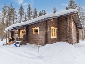 Une cabane en bois dont le toit est recouvert de neige, entourée d’arbres.