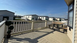 A deck with a picnic table and potted plants, overlooking mobile homes. - StaticHome-Sleeps6-Lakeview-Balcony-Parking-PetsOK (Mablethorpe)