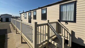 A row of mobile homes with a wooden deck and a staircase leading to the entrance. - StaticHome-Sleeps6-Lakeview-Balcony-Parking-PetsOK (Mablethorpe)