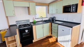 A compact kitchen with a stove, oven, microwave, and sink. - StaticHome-Sleeps6-Lakeview-Balcony-Parking-PetsOK (Mablethorpe)