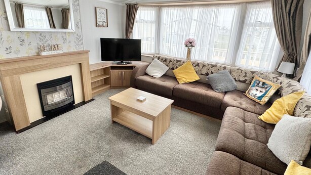 A living room with a sofa, coffee table, fireplace, television, and large windows with curtains. - StaticHome-Sleeps6-Lakeview-Balcony-Parking-PetsOK (Mablethorpe)