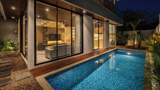 Una casa moderna con piscina, puertas de vidrio grandes y un interior muy iluminado.