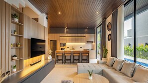 Una sala moderna con un sofá, una mesa de centro y un televisor. Cuenta con una zona de cocina con una mesa de comedor y sillas.