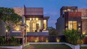 Una casa moderna de dos pisos con fachada de piedra, ventanas grandes y un jardín bien cuidado.