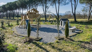 A playground with a wooden house, swings, and a slide, surrounded by trees and a gravel path. - Lavanda by Interhome (Fucecchio)