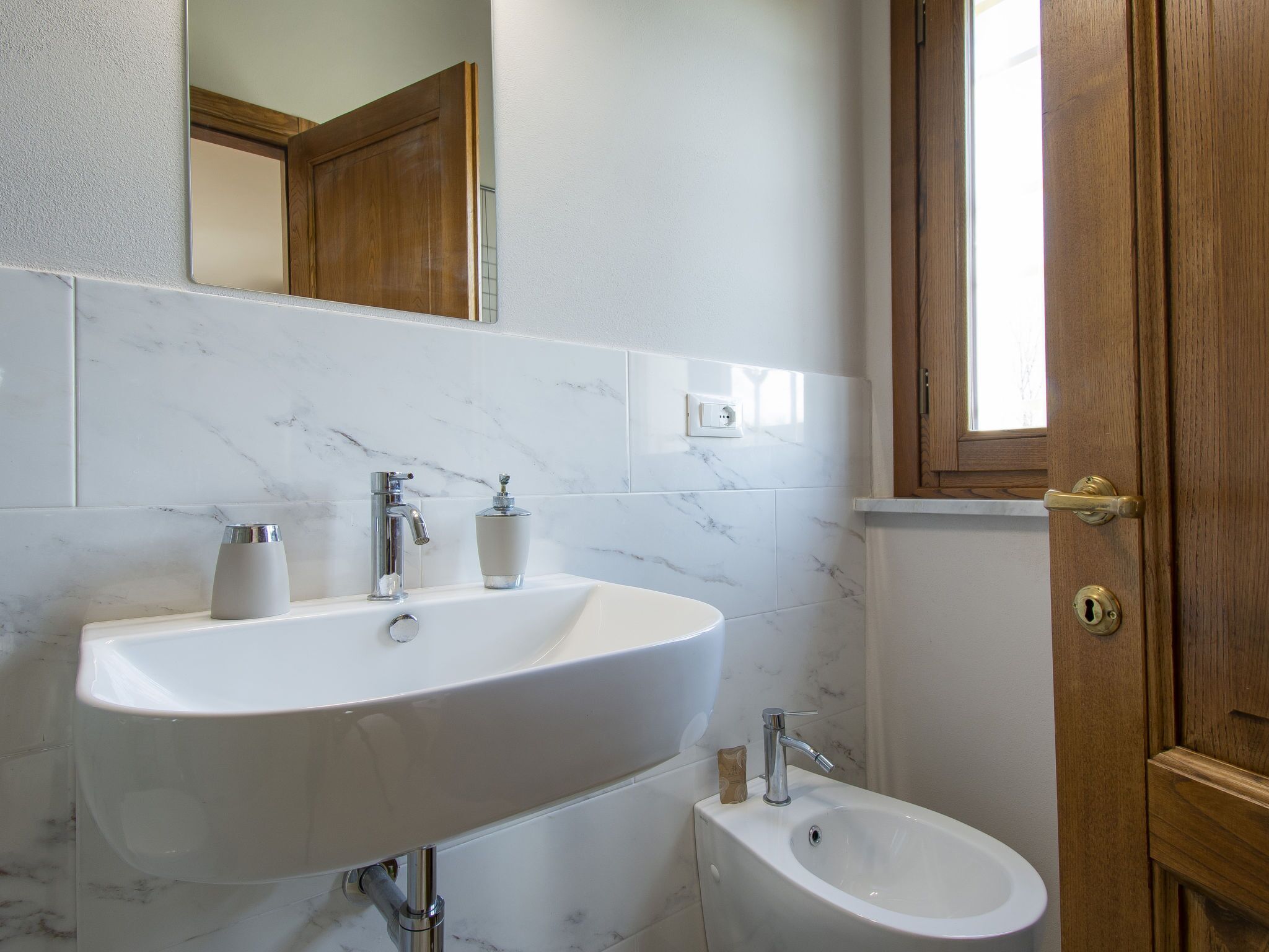 A bathroom with a large white sink, a mirror, and a wooden door.