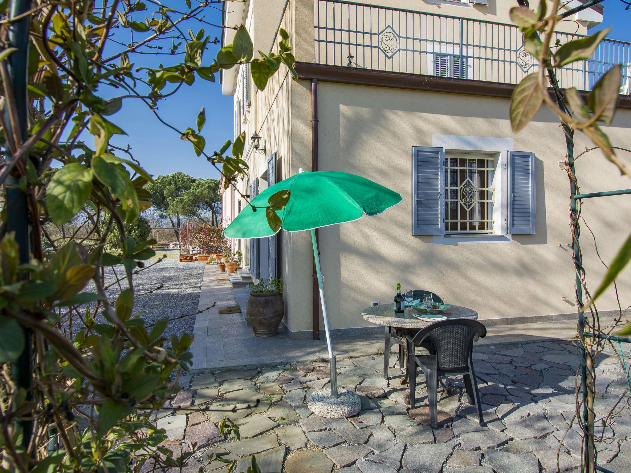 A stone-paved patio with a table and chairs, a green umbrella, and potted plants.
