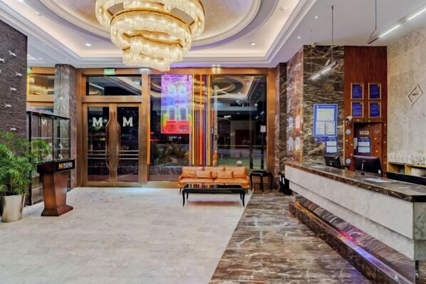 A hotel lobby with a reception desk, a bench, and a chandelier.