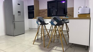 Una cucina moderna con frigorifero, microonde e pensili in legno. Due sgabelli da bar con motivo a scacchi.