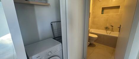 A compact bathroom with a washing machine, a toilet, and a bathtub.